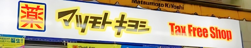 マツモトキヨシの白い店頭看板。左に青枠の「薬」ロゴ、中央に黄色で縁取った「マツモトキヨシ」、右に「Tax Free Shop」の文字。免税対応のドラッグストア。