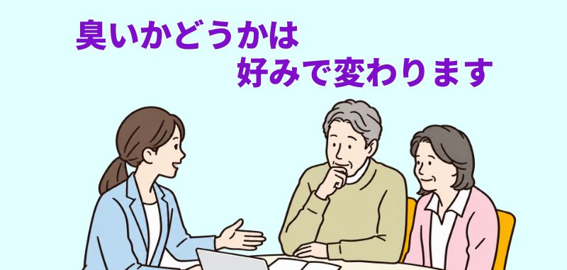 水色の背景にテーブルを挟んだ3人の人物が描かれ、上部に紫色のテキスト「臭いかどうかは 好みで変わります」が添えられたイラスト。若手の女性が年配の男女に説明している場面。